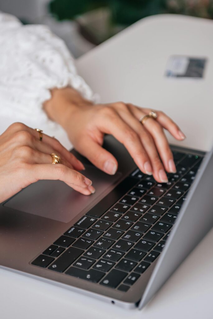 Hands of a woman typing on a laptop keyboard indoors, showcasing rings and fashion.
